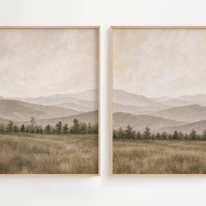 May include: A set of two vertical wall art prints in light wood frames, each depicting a landscape with a grassy field in the foreground, a line of trees in the mid-ground, and layers of hazy, muted beige and brown mountains in the distance.