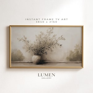 May include: A framed digital art print featuring a vase of leafy branches in neutral tones. The artwork has a gold frame and the text "INSTANT FRAME TV ART 3840 x 2160" and "LUMEN GALLERY". The overall aesthetic is soft and muted.