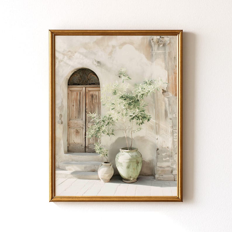 May include: A framed print featuring a sunlit courtyard scene. The artwork depicts a weathered wooden door beneath an arched opening, with a small vase and a large green pot holding a plant with light green foliage. The frame is gold.