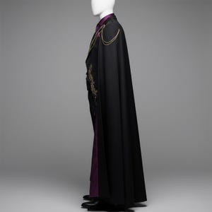 K&ouml;nnte beinhalten: Ein bodenlanger schwarzer Umhang &uuml;ber einer schwarzen Jacke mit goldener Stickerei und einem violetten Hemd. Der Umhang hat goldene Kettenakzente an den Schultern. Das Ensemble wird auf einer Schaufensterpuppe pr&auml;sentiert.