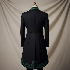 May include: Black formal coat with green embroidered trim on the collar and hem. The coat has a long, tailored design with a pleated back and button details. The coat is displayed on a mannequin.