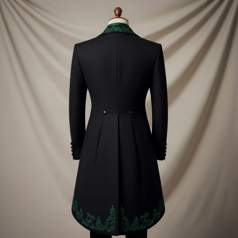 May include: Black formal coat with green embroidered trim on the collar and hem. The coat has a long, tailored design with a pleated back and button details. The coat is displayed on a mannequin.
