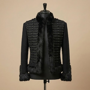 May include: Black military-style jacket with faux fur trim on the collar, front, and cuffs. The jacket features rows of decorative buttons and black fabric detailing. The jacket is displayed on a mannequin.