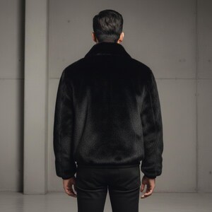 May include: A black faux fur bomber jacket with a classic collar and ribbed cuffs and hem. The jacket is shown from the back, with a focus on the texture and sheen of the fur. The jacket is paired with black pants.