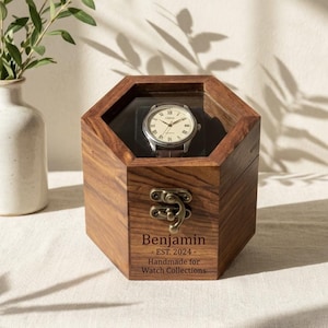 May include: A wooden watch display box with a clear top, holding a silver wristwatch with a cream-colored face. The box is engraved with "Benjamin - EST. 2024 - Handmade for Watch Collections."