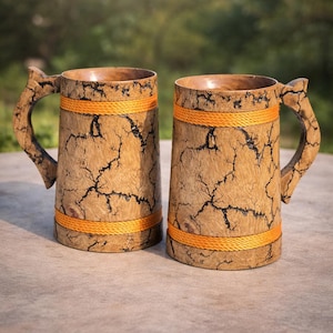 Könnte beinhalten: Zwei Bierkrüge aus Holz mit rustikalem Design. Die Krüge haben eine hellbraune Farbe mit dunklen Rissen und orangefarbenen Seilakzenten. Jeder Krug hat einen Griff aus dem gleichen Holz.