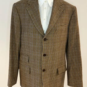 以下が含まれることがあります： 茶色とベージュのチェック柄ブレザーと、下に白い襟付きシャツ。 ブレザーには3つの茶色のボタンと2つのフロントポケットが付いています。 パターンは、小さな繰り返しのチェックデザインです。