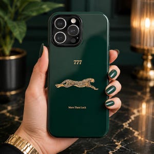 May include: A dark green smartphone case featuring a gold-colored graphic of a running cheetah in the center. Above the cheetah is the number 777 in gold, and below it is the text More Than Luck in gold lettering. The case has a camera cutout.