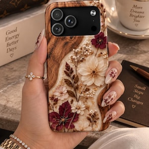 May include: A smartphone case featuring a wood grain pattern on the left side and a cream-colored resin section on the right. The case is decorated with embedded pressed flowers in shades of deep burgundy, soft pink, and white, with small sprigs.