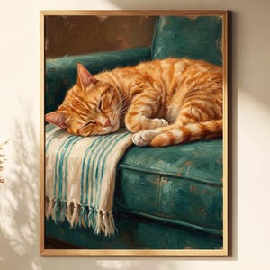 May include: A framed painting depicts a sleeping orange tabby cat curled up on a teal green armchair. The cat rests on a striped blanket with fringe. The artwork is in a wooden frame and is displayed in a cozy, well-lit room.