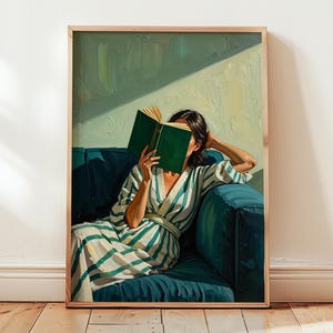 May include: A framed art print depicts a person reading a book while seated on a teal sofa. The person is wearing a striped robe. The background features a light green wall and a wooden floor.