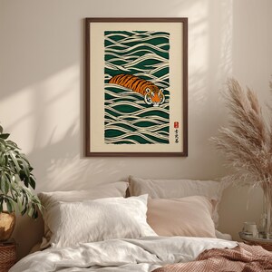 May include: Framed art print featuring a tiger swimming in stylized green waves. The tiger has orange and black stripes and is centered in the artwork. The print has a cream-colored background and a dark brown frame. Japanese text is in the lower right corner.