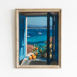 May include: A framed painting depicting an open window with bright blue shutters looking out over a deep blue sea with sailboats. A small citrus tree with vibrant orange fruit sits on the windowsill, casting shadows against the white wall.