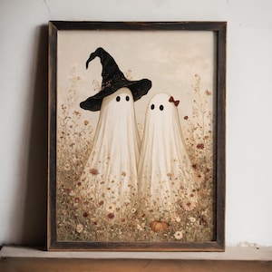 May include: A framed wall art print featuring two white ghost figures standing in a field of wildflowers. One ghost wears a black witch hat, and the other has a small red bow. A single orange pumpkin sits at their feet in the muted floral meadow.