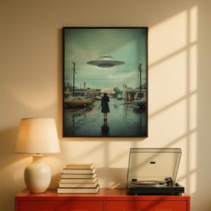 May include: Framed art print showing a person with an umbrella in a rainy street scene, with a diner and a UFO above. The artwork is in a black frame, with a vintage style and muted colours.