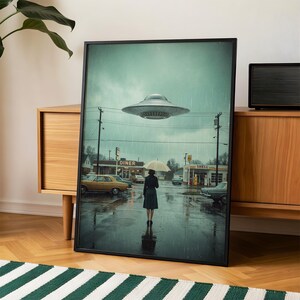 May include: A framed art print showing a rainy street scene with a diner, petrol station, and a person with an umbrella. A silver UFO hovers overhead. The artwork has a vintage, retro aesthetic.