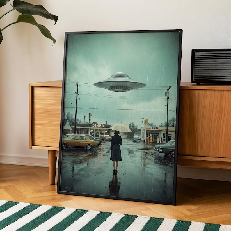 May include: A framed art print showing a rainy street scene with a diner, petrol station, and a person with an umbrella. A silver UFO hovers overhead. The artwork has a vintage, retro aesthetic.