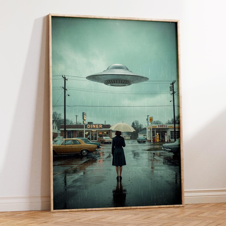 May include: A framed art print shows a retro diner scene under a rainy sky, with a UFO hovering above. A person with an umbrella stands in the street. Classic cars and a Shell petrol station are also visible.