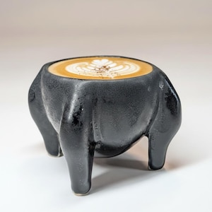 May include: A set of three ceramic mugs with a speckled, matte finish. The mugs are in shades of cream, light gray, and dark gray. Each mug has a simple, modern design and a rounded handle. The mugs are stacked on top of each other.