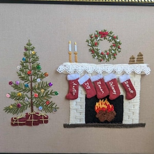 以下が含まれることがあります： 刺繍されたクリスマスのシーン。装飾された木、靴下の暖炉、リースが描かれています。木にはカラフルなオーナメントが飾られ、プレゼントの隣にあります。暖炉には名前が書かれた5つの赤い靴下があります。お祝いのホリデーデコレーション。