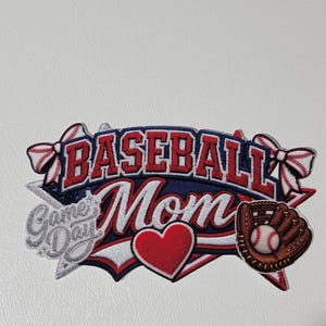May include: Embroidered patch with the words "Baseball Mom" in red and white lettering on a navy blue background. Features a red heart, baseball glove, and the words "Game Day".