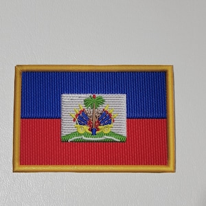 May include: Embroidered patch featuring the flag of Haiti. The rectangular patch has a blue upper half and a red lower half, with a white central panel displaying the Haitian coat of arms. The patch is bordered with gold thread.