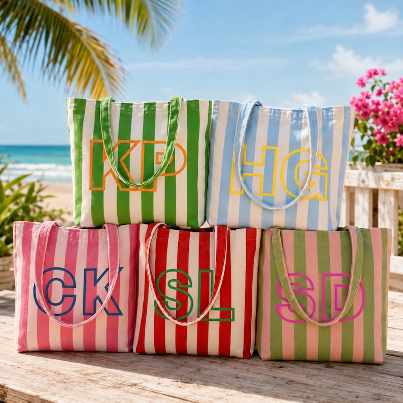 May include: Five canvas tote bags with vertical stripes in green, light blue, pink, and red. Each bag features two shoulder straps and a large, bold, two-letter monogram in a contrasting color, including KP, HG, CK, SL, and SD, printed on the front.