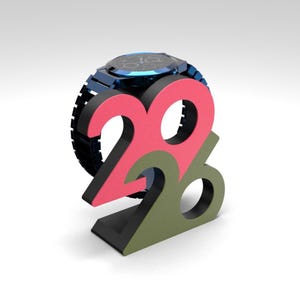 May include: A blue wristwatch with a black band rests atop a colorful 2026 display. The numbers are in pink and green, with a black base. The watch has a blue face and a blue metal band.