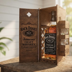 Könnte beinhalten: Eine Holzkiste mit einer Flasche Tennessee Craft Whiskey und drei Schnapsgläsern. Die Whiskeyflasche hat ein schwarzes Etikett mit weißem Text. Die Kiste ist mit den Worten "Hack Daniel" und "No. 7" graviert.