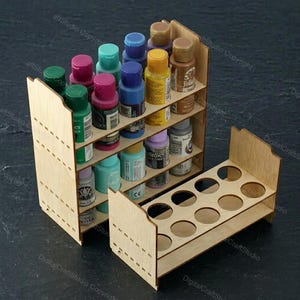 Puede incluir: Un estante de almacenamiento de pintura de madera con múltiples estantes y un soporte separado. El estante está lleno de varios colores de botes de pintura. El diseño es de madera clara, con una apariencia limpia y organizada.