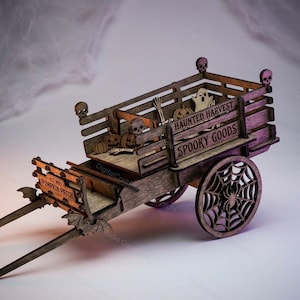 Op de afbeelding: Een houten wagen met een donkere afwerking en lasergesneden details, waaronder spinnenwebwielen, vleermuisaccenten en schedels. De zijpanelen zijn gegraveerd met de tekst "HAUNTED HARVEST" en "SPOOKY GOODS" en de voorzijde toont "PUMPKIN PATCH."