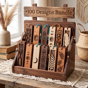 Op de afbeelding: Een houten displaystandaard met de tekst +100 Designs Bundle, met een collectie rechthoekige houten bladwijzers. Elke bladwijzer toont ingewikkelde lasergesneden patronen, waaronder dromenvangers, zonnen, manen en botanische motieven.