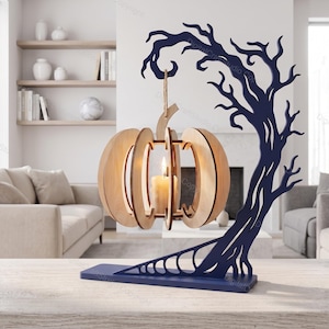 Op de afbeelding: Een donkerblauwe houten standaard in de vorm van een kale boom met een hangende lichtgekleurde houten pompoenlantaarn. De pompoenstructuur is gemaakt van verticale latten en bevat een witte stompkaars in het midden, opgehangen aan een touw.