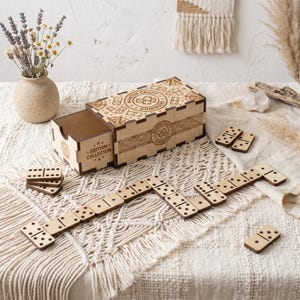 Peut inclure: Un jeu de dominos en bois avec une boîte de rangement coulissante portant l'inscription gravée au laser Master Craft Dominoes et Edition Collector. Le jeu comprend plusieurs tuiles rectangulaires à points noirs disposées en zigzag.