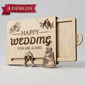 Peut inclure: Une boîte coulissante en bois clair avec des motifs gravés au laser, dont deux oiseaux sur une branche, deux alliances, deux flûtes à champagne et un gâteau à étages. Le texte indique "HAPPY WEDDING FOR MR. & MRS." et "EST. 2024".