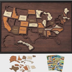 May include: A framed wooden wall map of the United States featuring laser-cut state pieces in various wood tones. The map includes individual state cutouts and a collection of colorful illustrated stickers representing different regions of the country.