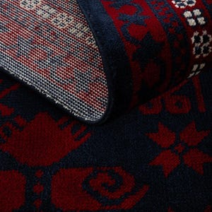 May include: A rolled-up area rug with a dark blue background and a repeating pattern in red and white. The rug's design includes floral and geometric motifs, creating a traditional aesthetic. The edges are finished with a dark blue border.