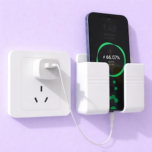May include: A white wall-mounted phone holder with a charging cable connected to a white electrical outlet. A black smartphone is in the holder, displaying a charging screen. The background is a light purple wall.