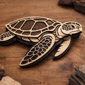 May include: Wooden sea turtle figurine with intricate laser-cut details. The turtle features a light brown shell with a textured pattern, dark brown accents, and black outlines. The figurine is set against a wooden background.