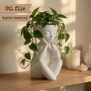 May include: A white ceramic planter shaped like a person sitting with their head resting on their hands, filled with a trailing green pothos plant. The text Stl file and digital download is visible in the upper left corner of the image.
