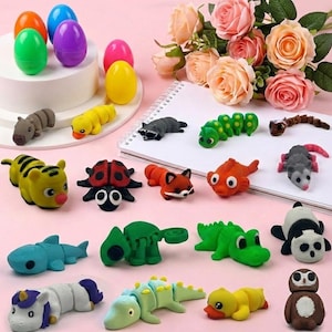 May include: A collection of colorful animal-shaped erasers and egg-shaped containers. The erasers include a tiger, ladybug, fox, fish, alligator, panda, and more. The background features a pink surface and a bouquet of roses.