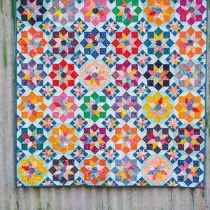 Puede incluir: Una colcha rectangular con un patr&oacute;n repetitivo de bloques de estrellas multicolores en tonos rojo, naranja, amarillo, verde, azul, morado y rosa. Las estrellas est&aacute;n sobre un fondo azul claro con un borde de color azul s&oacute;lido.