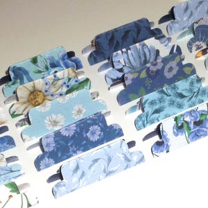 Puede incluir: Un surtido de pestañas de papel con estampado floral azul. Las pestañas presentan varios tonos de azul y blanco con diferentes diseños florales, incluyendo margaritas y otras flores. Las pestañas están dispuestas en filas.