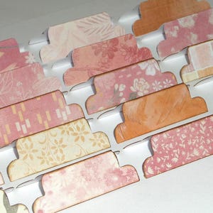 Könnte beinhalten: Dekorative Papierregisterkarten mit verschiedenen floralen und geometrischen Mustern in Rosa-, Pfirsich- und Cremetönen. Die Registerkarten sind in Reihen angeordnet, ideal zum Organisieren oder Basteln.