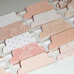 May include: Close-up of decorative paper tabs in various shades of pink and white. The tabs feature different patterns, including polka dots, floral designs, and geometric shapes. These tabs are ideal for scrapbooking or organizing.