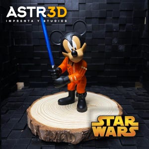 May include: A Mickey Mouse figurine in an orange Star Wars outfit, holding a blue lightsaber. The figure is displayed on a wooden slice, with the Star Wars logo. The background is a dark, textured wall. The text "ASTR3D" is at the top.