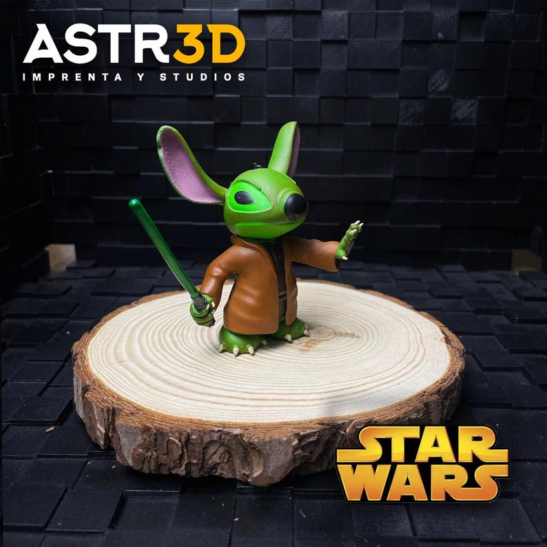May include: A green figurine of a character with large ears, wearing a brown coat and holding a green lightsaber. The figurine is on a wooden slice, with the Star Wars logo visible. The text "ASTR3D IMPRENTA Y STUDIOS" is at the top.