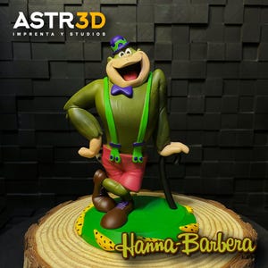 May include: A green cartoon character figurine with a purple bow tie, suspenders, and hat, and red shorts. The figurine is standing on a green base with yellow bananas and the Hanna-Barbera logo. The ASTR3D logo is in the top left.