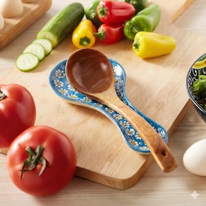 May include: A wooden spoon rests on a blue and white floral spoon rest. Fresh vegetables, including tomatoes, cucumbers, and bell peppers, are arranged on a wooden cutting board, suggesting a culinary theme.