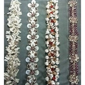 May include: Close-up of four decorative beaded trims. The trims feature various designs with white, silver, red, and purple beads and sequins. The trims are arranged vertically against a gray background.
